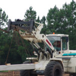 Backhoe forklife carrying large concrete block on chains